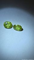 Two oval chartreuse sphene gemstones under spotlight