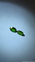 Two oval electric green chrome diopside gemstones on neutral background