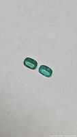 Pair of cushion cut green emeralds on neutral background