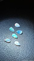 Six pear-cut opals on black textured surface showing play of color