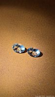 Pair of pale blue oval faceted gemstones on brown surface