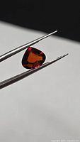 Triangular faceted garnet held by tweezers showing color and shape