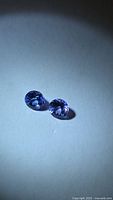 Both round blue-purple tanzanite gemstones on neutral background
