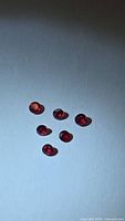Six round vivid red rubies on neutral background.