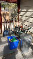 Wide view of long-handled tools, cart, trash can, blue tote