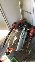 Group shot showing all power yard tools on floor: hedge trimmer, Yardworks blower/vac, Stihl string trimmer and red/orange gas blower