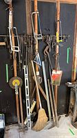 Wide shot of wall-mounted tools: pry bars, hacksaws, levels, square, broom, saw blade, bucket of blades