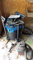 Large blue/black vacuum with wands, hose, manual and small red vacuum beside it