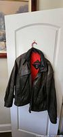 Front view of dark brown leather bomber jacket on hanger showing overall style and condition