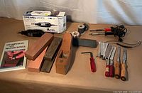 All items laid out including Dremel, plane, stones, soldering irons, chisels, saw blades, book