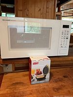 Front view of Sharp Carousel microwave with boxed Dash waffle maker in front