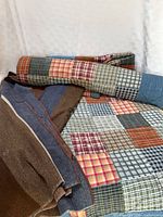 Rolled plaid patchwork quilt beside folded wool blanket and second quilt