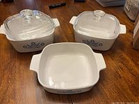 Three square CorningWare dishes with two lids displayed on table