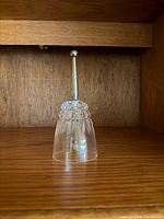 Full view of the clear crystal bell standing on wood shelf