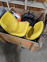 Crate containing two yellow tractor seats, black seat pan, orange pail with bottles