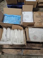 Overview of several open cartons containing individually wrapped white and blue disposable gowns