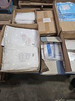 Open cartons on pallet showing sealed white gowns in plastic