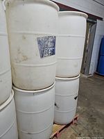 Four stacked white plastic barrels with label remnants and grime