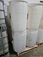 Stacked white plastic drums on pallet showing size and condition