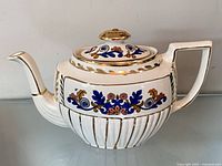 Left side view of white ceramic teapot with lid showing floral design and gold trim