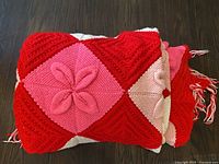 Folded afghan showing red and pink diamond squares with raised flower, fringe visible