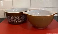 Two brown Pyrex mixing bowls, one with floral pattern, one solid