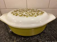 Side view of olive-green casserole with patterned white lid
