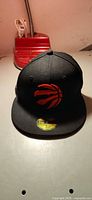 Front view of black New Era Raptors hat displaying logo and brim sticker