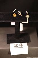 Three jewellery pieces displayed on black stand: left Houdry pin, centre pearl stud, right pendant