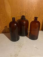 Front view of all three large amber glass bottles standing on floor