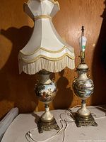 Two matching ornate porcelain table lamps, one with fabric shade, one without