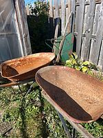 Two rusted steel tray wheelbarrows side by side, frames and handles visible
