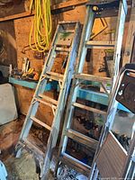 Two full-size aluminum ladders leaning against wall
