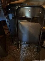 Two black metal folding chairs leaning together showing backs and vinyl seats