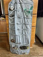 Front side of grey hanging organizer with numerous jewellery pieces in clear pockets