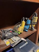 Four handheld corded tools on shelf (drills, jigsaw, grinder)