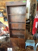 Front view of tall brown-stained bookcase beside blue stool
