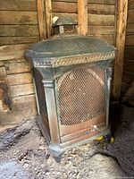 Front view of square metal fire pit showing mesh panel, decorative trim, rust and dust