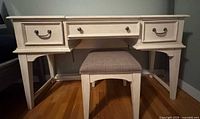 Front view of off-white three-drawer vanity desk with matching stool