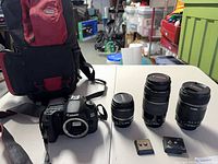 Group shot of camera body, three lenses, battery charger, tripod plate, and backpack