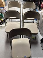 Front view of the five beige metal folding chairs folded open