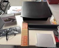 All items on tabletop: printer stand, boxed Brookstone scanner, USB keyboard, cable raceway kit box, rubbermaid shelf panel, UniFi Switch 8