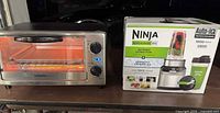 Toaster oven powered on next to boxed Ninja blender