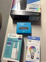 Four boxed smart-home/networking items: Netgear modem router, Echo Auto, TP-Link range extender, Feit smart bulb
