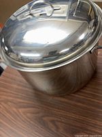 Side view of stainless steel stock pot with lid showing handles and mirror finish