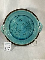Full view of turquoise earthenware dish with bird motif, brown rim, side handles, lot tag visible