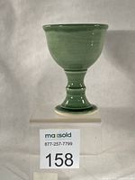 Front view of green celadon stoneware wine goblet on acrylic stand