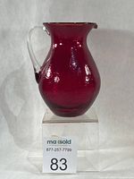 Front view of ruby crackle glass pitcher on display block with lot number
