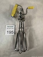 Full view of Maynard egg beater showing yellow handle, dual stainless beaters, and size reference card