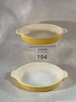 Two yellow Pyrex #700 dishes front view on stand with lot tag